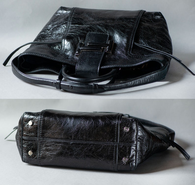 Op de afbeelding: Zwarte leren tote bag met een zilveren gesp en een bovenste handvat. De tas heeft een textuur en een verweerde look.