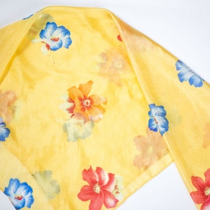 May include: A yellow silk scarf with a floral print featuring red, orange, blue, and white flowers.