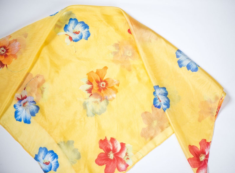 May include: A yellow silk scarf with a floral print featuring red, orange, blue, and white flowers.