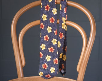 May include: A dark blue silk tie with a floral pattern of yellow and orange flowers. The tie is hanging on a wooden chair.
