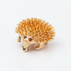 May include: A gold-toned brooch in the shape of a hedgehog with brown rhinestone eyes.