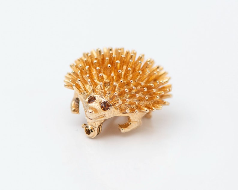 May include: A gold-toned brooch in the shape of a hedgehog with brown rhinestone eyes.