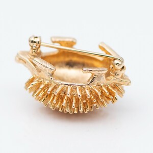 May include: A gold-toned brooch in the shape of a hedgehog. The hedgehog is made of metal and has a textured surface. The brooch has a pin on the back for attaching it to clothing.