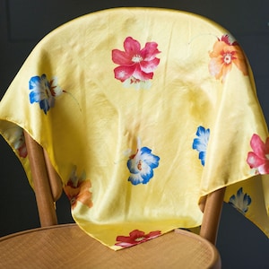 May include: A yellow silk scarf with a floral pattern. The scarf features red, blue, and orange flowers on a yellow background.