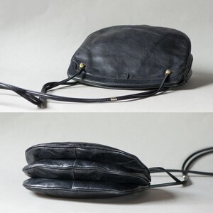 Puede incluir: Bolso bandolera de cuero negro con forma redondeada y una correa larga y fina. El bolso presenta detalles dorados y una superficie texturizada. El dise&ntilde;o del bolso incluye una construcci&oacute;n en capas y la correa es ajustable.
