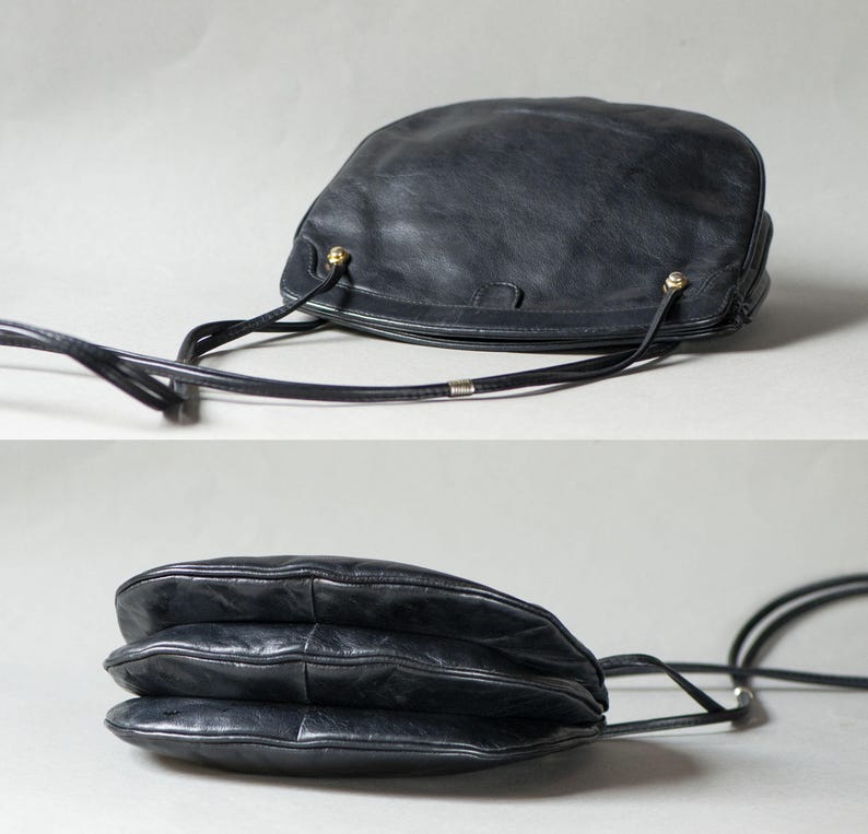 Puede incluir: Bolso bandolera de cuero negro con forma redondeada y una correa larga y fina. El bolso presenta detalles dorados y una superficie texturizada. El dise&ntilde;o del bolso incluye una construcci&oacute;n en capas y la correa es ajustable.