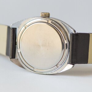 May include: A silver wristwatch with a black leather band. The watch face is covered with a silver metal case.