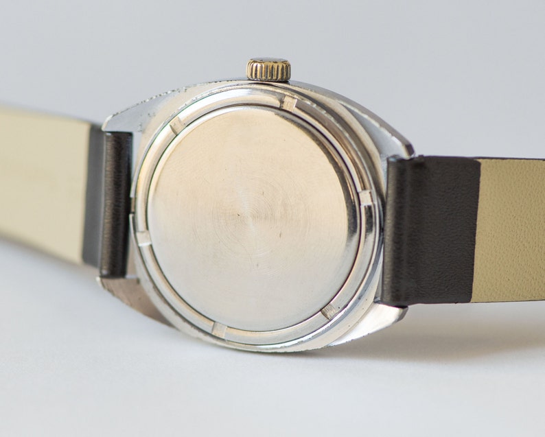 May include: A silver wristwatch with a black leather band. The watch face is covered with a silver metal case.