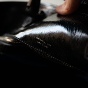 Op de afbeelding: Close-up van een zwarte leren tas met een zilveren rits en de tekst "Genuine Leather Made in Italy" gegraveerd aan de binnenkant.