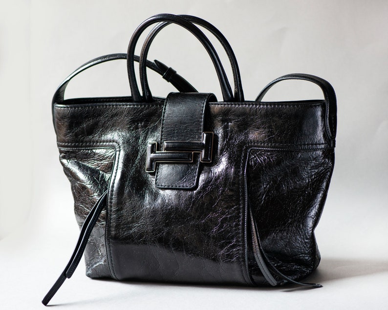 En sort Tod's-lædertaske med sølvspændelukning. Tasken har en tekstureret læderfinish og en lang rem. Den har en fremtrædende tonet Double T-logo-læderapplikationslukning på tværs af den forreste fane. Inkluderer en sekundær lang, flad læderskulderrem for alsidig styling.