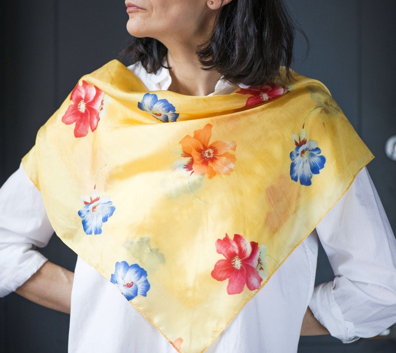 May include: A yellow silk scarf with a floral print. The flowers are red, orange, blue, and white.