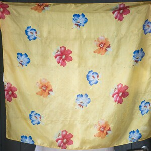 May include: A yellow silk scarf with a floral pattern. The flowers are red, blue, and orange.