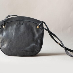 Puede incluir: Bolso bandolera de cuero negro con la parte superior curvada y una correa larga y fina. El bolso presenta detalles dorados en las fijaciones de la correa. Un estilo cl&aacute;sico, adecuado para el uso diario.