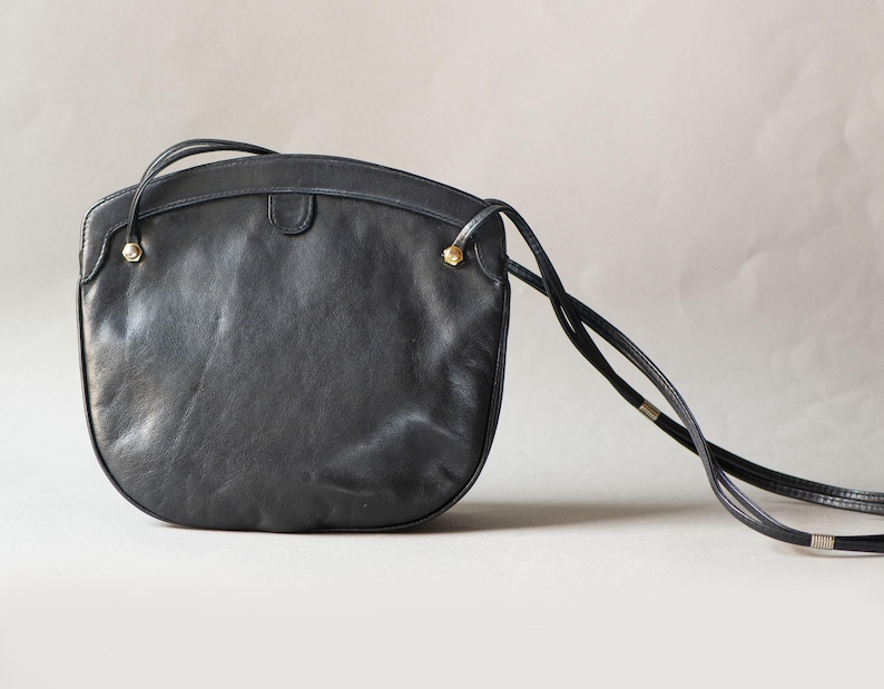 Puede incluir: Bolso bandolera de cuero negro con la parte superior curvada y una correa larga y fina. El bolso presenta detalles dorados en las fijaciones de la correa. Un estilo cl&aacute;sico, adecuado para el uso diario.