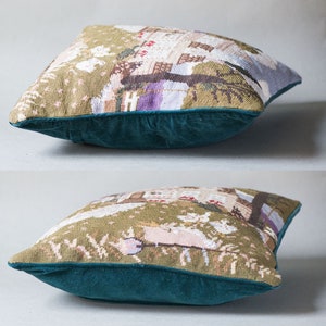 May include: A green and brown tapestry cushion with a detailed embroidered scene of a house and trees. The cushion has a dark teal velvet border.