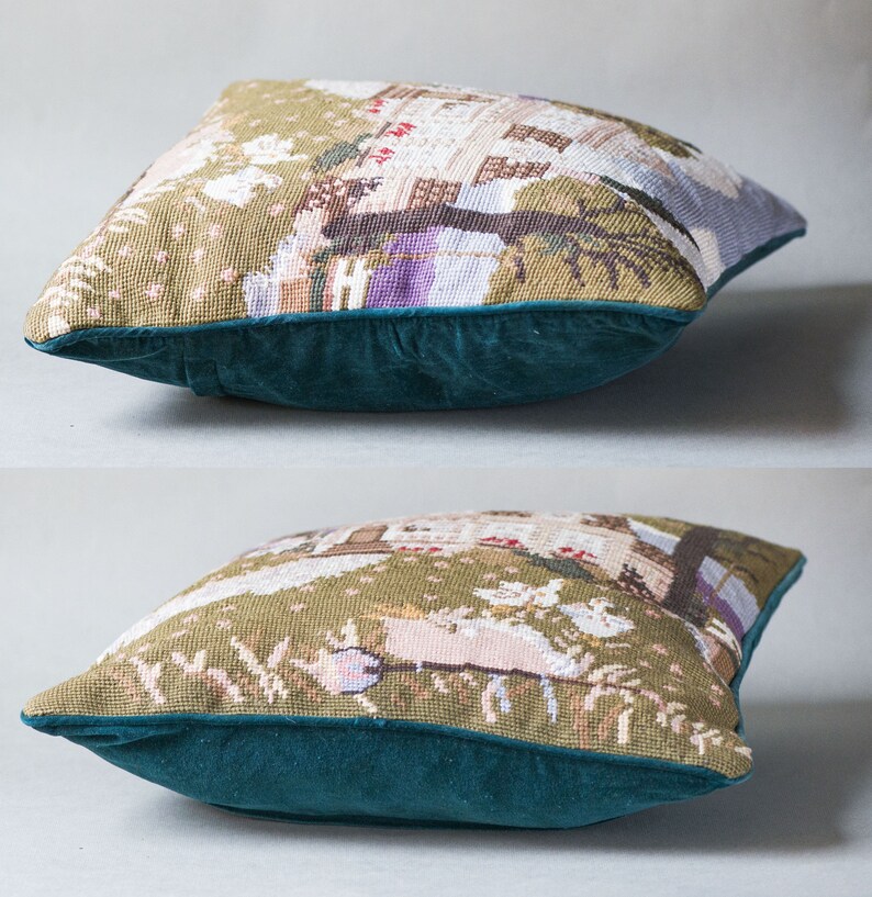 May include: A green and brown tapestry cushion with a detailed embroidered scene of a house and trees. The cushion has a dark teal velvet border.