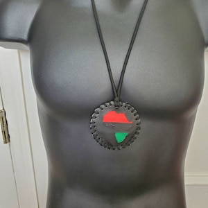 Peut inclure: Un collier en cuir noir avec un pendentif rond représentant un contour rouge, vert et noir du continent africain.