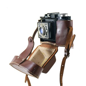May include: A vintage black Ultra Six camera with a brown leather case and a strap. The camera has a lens cap and a viewfinder.