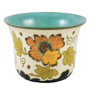 Pode incluir: Um vaso de cerâmica branco com uma borda verde-azulada e um design floral com flores e folhas laranja, amarelas e verdes.