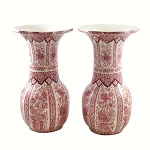 May include: Two matching decorative vases with a cream background and a red floral pattern. The vases have a flared top and a bulbous body. The floral design includes flowers and leaves. The vases are likely made of ceramic.