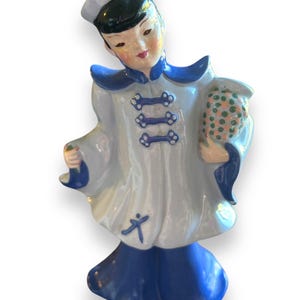 May include: A blue and white ceramic figurine of a person wearing a traditional Chinese robe and hat. The figurine is holding a bouquet of flowers.