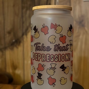 May include: A frosted glass water bottle with a bamboo lid and a straw. The bottle has a design of yellow ducks wearing top hats and red apples. The text "Take that DEPRESSION!" is printed on the bottle.