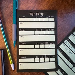 May include: Black character sheets with white text and boxes for role-playing games. The text "The Party" is at the top. A teal pencil and a rainbow pencil are on the wooden surface.