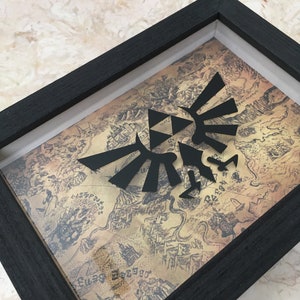 May include: A framed print of a black and white Triforce symbol on a vintage map background. The frame is black wood.