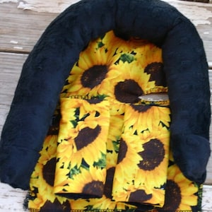 May include: Black and yellow sunflower fabric baby head support pillow. The pillow is shaped like a horseshoe and has a soft, plush lining.