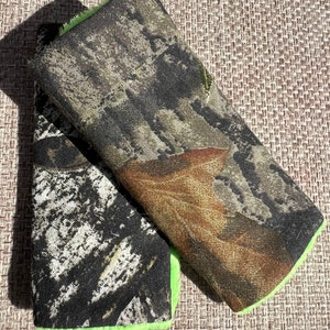 May include: Two camouflage fabric patches with a bright green trim. The patches are made of a soft, textured fabric and have a woodland camouflage pattern.