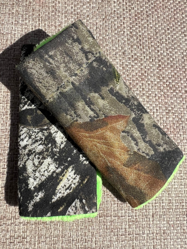 May include: Two camouflage fabric patches with a bright green trim. The patches are made of a soft, textured fabric and have a woodland camouflage pattern.