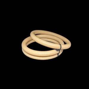 May include: Two ivory-colored bangles, stacked together, against a black background. The bangles are smooth and round, with a glossy finish. They are connected by a dark gray string.
