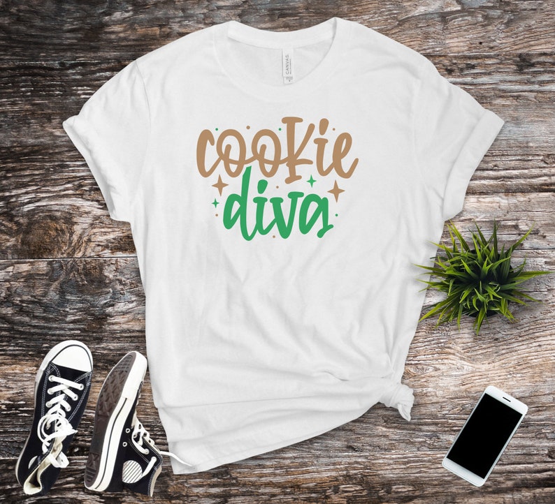 May include: White t-shirt with the text "cookie diva" in brown and green lettering with small gold stars.