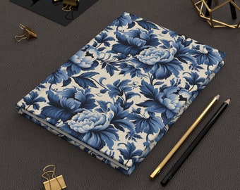 Puede incluir: Un cuaderno de color crema con un patrón floral azul y blanco. El cuaderno está cerrado y sobre una superficie gris oscuro.
