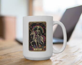 May include: White ceramic mug featuring a tarot card design. The card depicts a skeleton riding a unicorn under a rainbow, with the words "THE AUDACITY." The design has a vintage, gothic aesthetic.