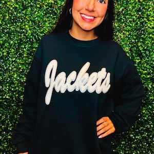 Puede incluir: Una sudadera negra con un gráfico blanco y brillante de "Jackets" en la parte delantera.