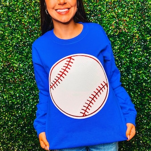 Può includere: Una felpa blu reale con una grafica di una palla da baseball bianca. La palla da baseball ha cuciture rosse.