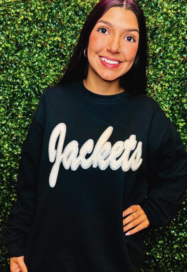 Puede incluir: Sudadera negra con un gr&aacute;fico blanco y brillante de "Jackets".