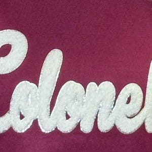 Puede incluir: Una sudadera color granate con la palabra "Colonels" en letras blancas y abultadas.
