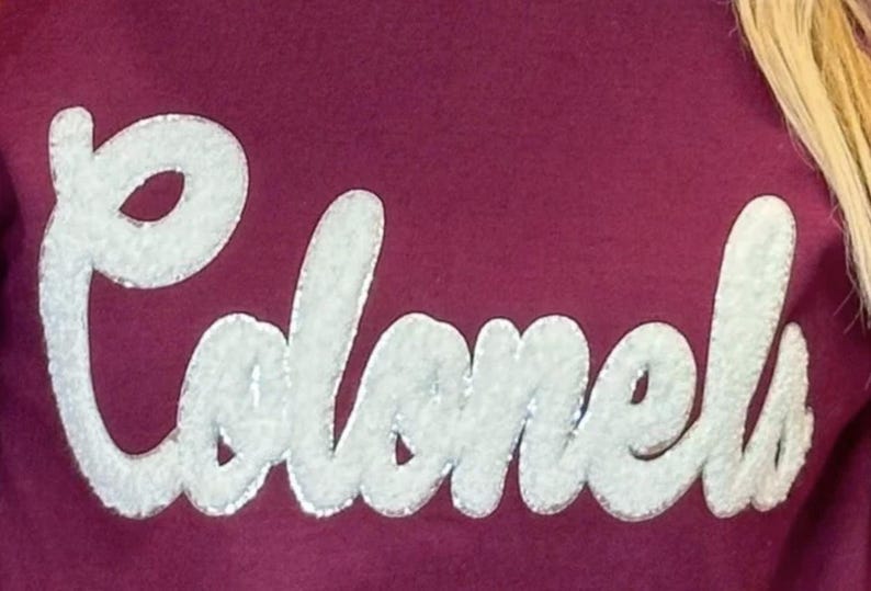 Puede incluir: Una sudadera color granate con la palabra "Colonels" en letras blancas y abultadas.
