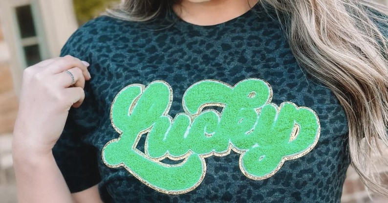 May include: A black and green leopard print t-shirt with a green and gold glitter "Lucky" graphic.