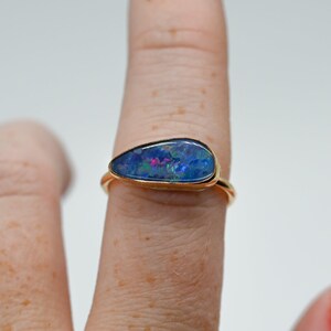 May include: A gold ring featuring a teardrop-shaped opal gemstone. The opal is a vibrant blue with flashes of green and red.
