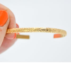 May include: A gold bangle bracelet with a delicate floral design.