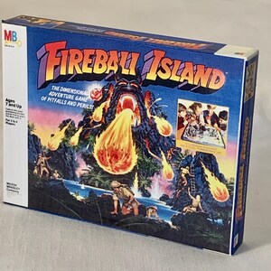 Może przedstawiać: Pudełko gry planszowej Fireball Island. Pudełko zawiera żywą ilustrację wulkanicznej wyspy z wybuchem ognia. Tekst na pudełku zawiera "Fireball Island" i "The Dimensional Adventure Game of Pitfalls and Perils." Wiek 7 lat i więcej.