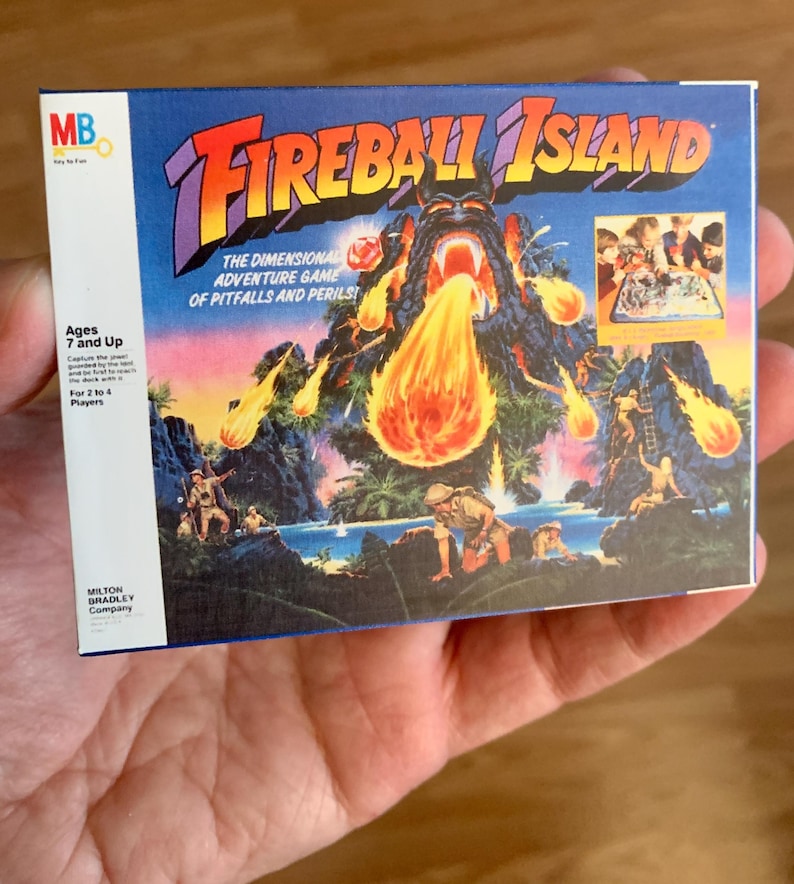Może przedstawiać: Vintage pudełko gry planszowej Fireball Island. Pudełko zawiera kolorową ilustrację wulkanicznej wyspy z erupcją ognia. Tekst zawiera "Fireball Island" i "The Dimensional Adventure Game of Pitfalls and Perils!". Dla os&oacute;b w wieku 7 lat i starszych.