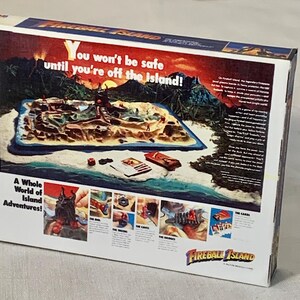 Może przedstawiać: Pudełko gry planszowej Fireball Island. Pudełko zawiera kolorową ilustrację wyspy z tekstem "You won't be safe until you're off the island!" i "A Whole World of Island Adventures!"