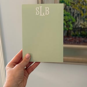 May include: A light green notepad with the monogram "SLB" printed in white on the front.