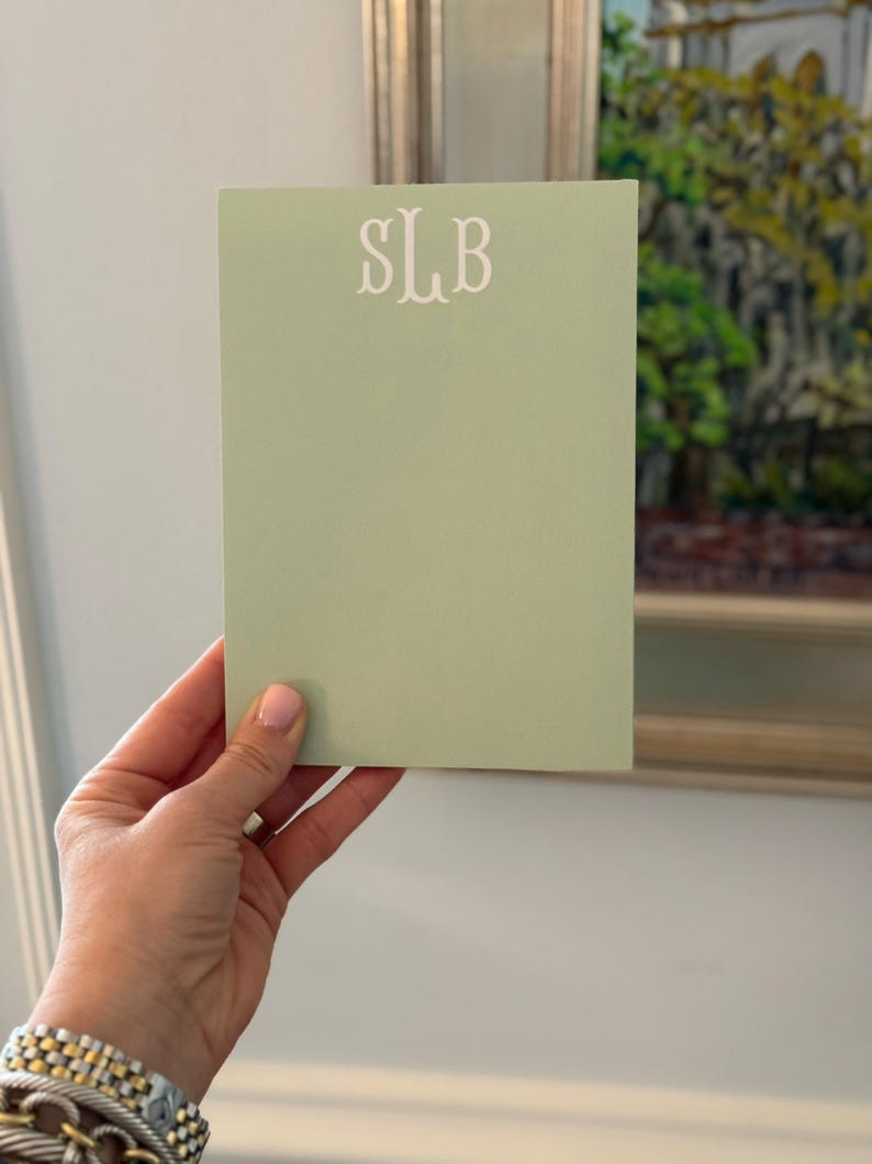 May include: A light green notepad with the monogram "SLB" printed in white on the front.