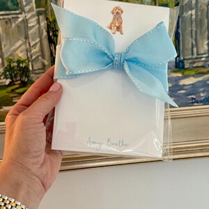Peut inclure: Un paquet de cartes blanches avec un n&oelig;ud bleu clair et une petite illustration d'un chien. Les cartes sont envelopp&eacute;es dans du cellophane transparent. Le nom "Amy Boothe" est imprim&eacute; en bas des cartes.