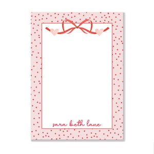 May include: Pink notepad with a red polka dot border and a red ribbon with two pink hearts. The notepad has the text "sara beth lane" at the bottom.